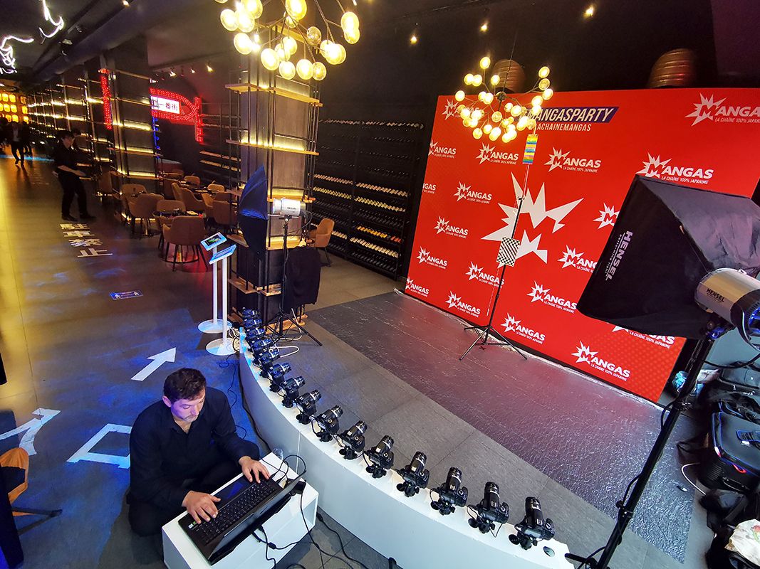Technicien à la régie devant un photocall rouge, arc d'appareils et éclairage en boîte à lumière