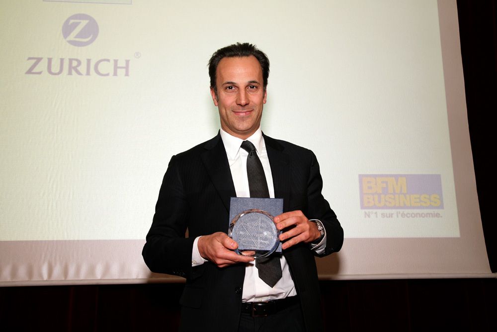 Lauréat en costume tenant son trophée devant l'écran de la cérémonie