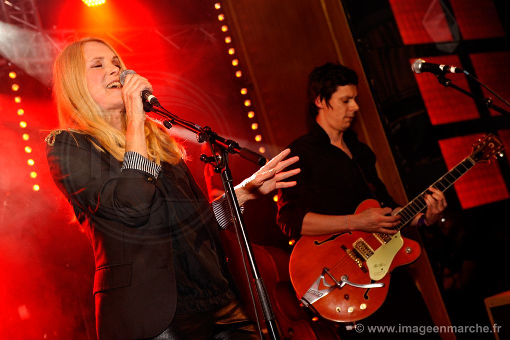 Chanteuse en robe noire et guitariste sur une scène baignée de lumière rouge