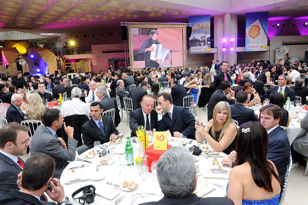 Dîner de convention aux tables rondes, convives attablés et écran géant au fond