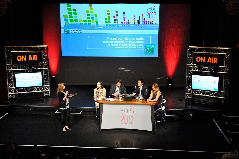 Plateau de talk-show avec panneaux « On Air », animatrice et intervenants autour d'une table