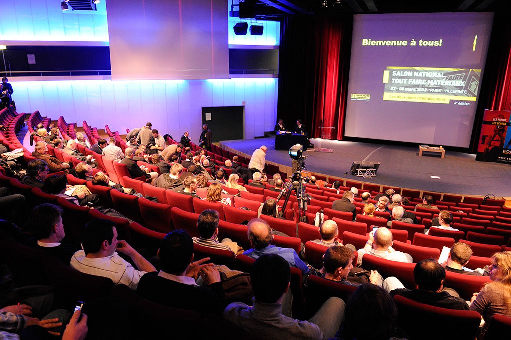 Amphithéâtre aux fauteuils rouges, écran affichant « Bienvenue à tous ! »