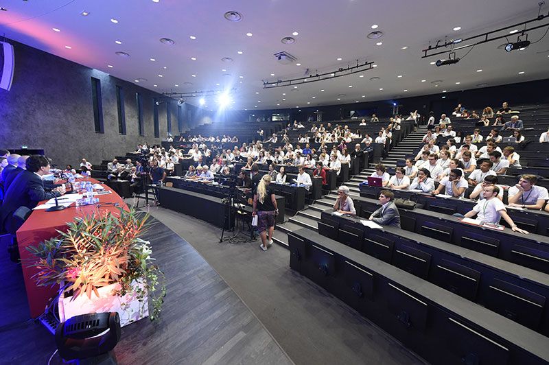 Grand amphithéâtre vu d'en haut, gradins remplis et table des intervenants
