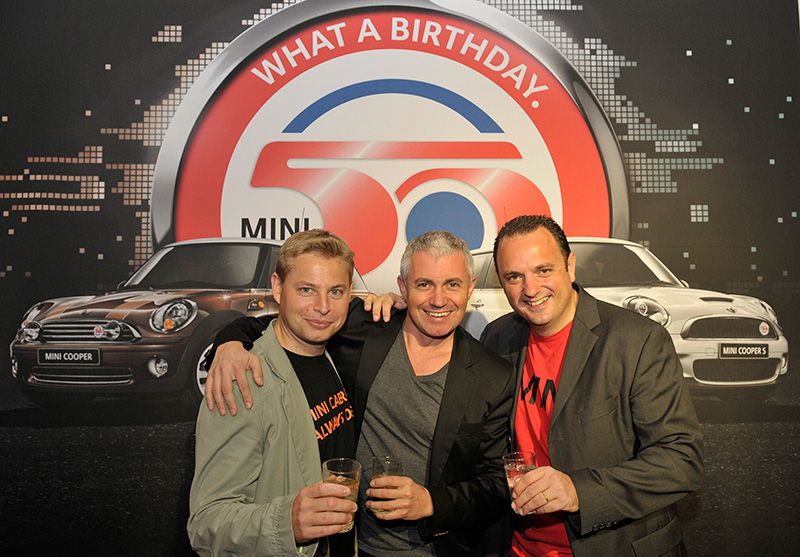 Trois invités trinquant devant le visuel « What a birthday » des 50 ans de la MINI