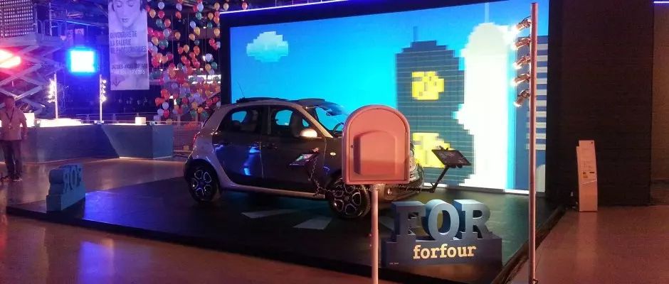 smart forfour exposée devant un mur d'écrans pixelisés, borne photo rouge à côté
