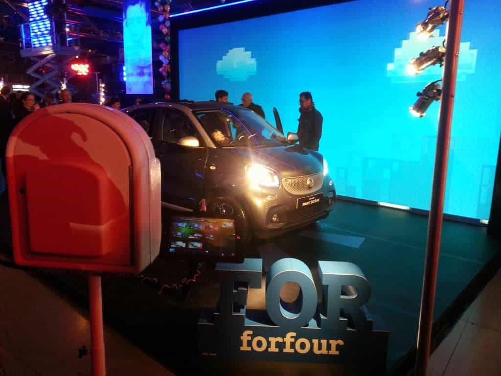 smart forfour phares allumés derrière les lettres géantes « FOR », borne photo au premier plan