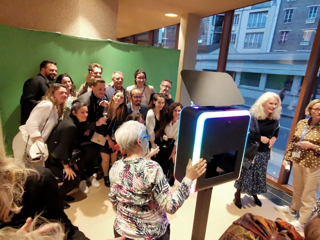 Groupe nombreux posant devant la borne photo près des baies vitrées