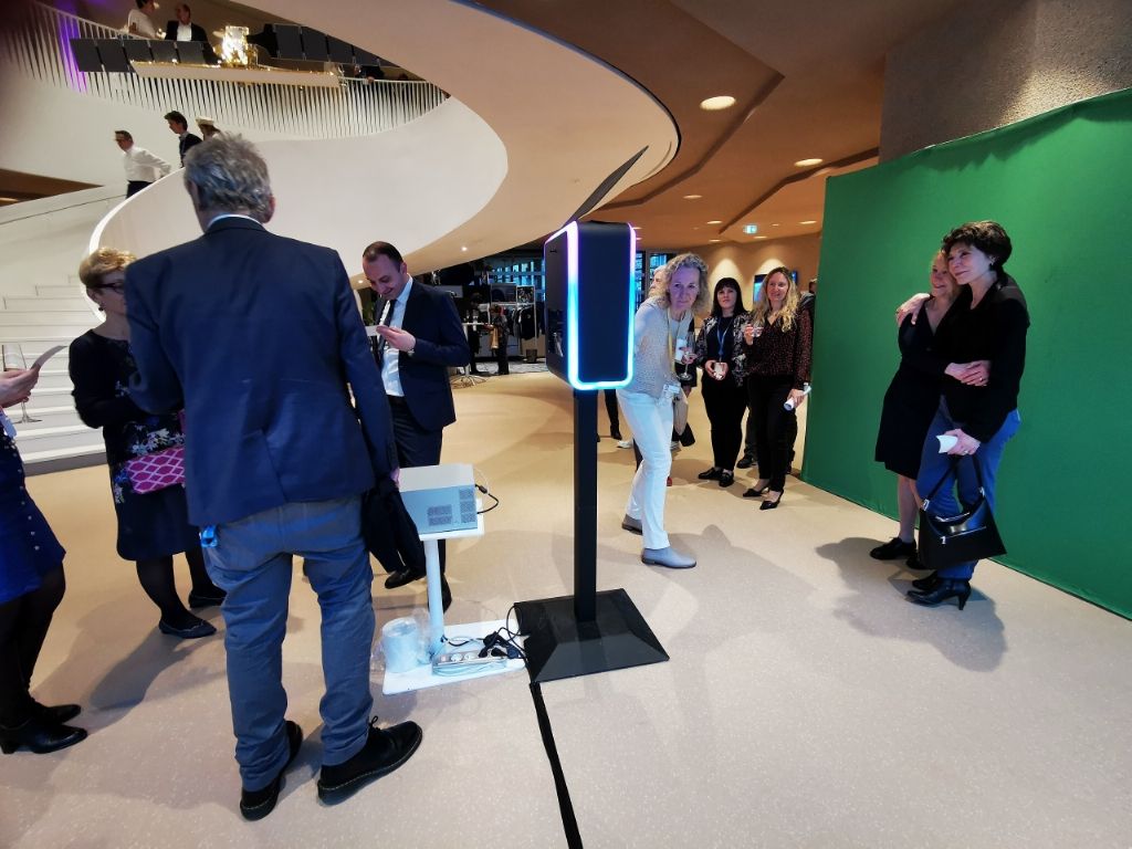 Hall vitré avec fond vert et borne photo lumineuse, invités en train d'arriver