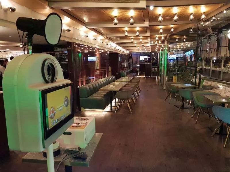 Borne photo installée à l'entrée d'une grande brasserie aux banquettes vertes