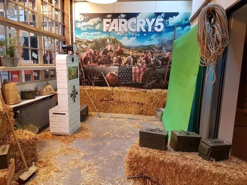 Borne photo en bois blanchi dans un décor Far Cry 5 avec bottes de paille et fond vert