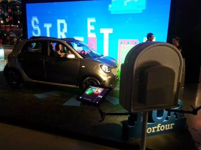Borne photo à côté d'une smart forfour exposée devant un écran géant aux graphismes pixelisés