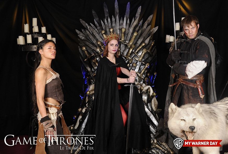 Invitée sur le trône de fer de Game of Thrones entourée de comédiens costumés et d'un loup géant