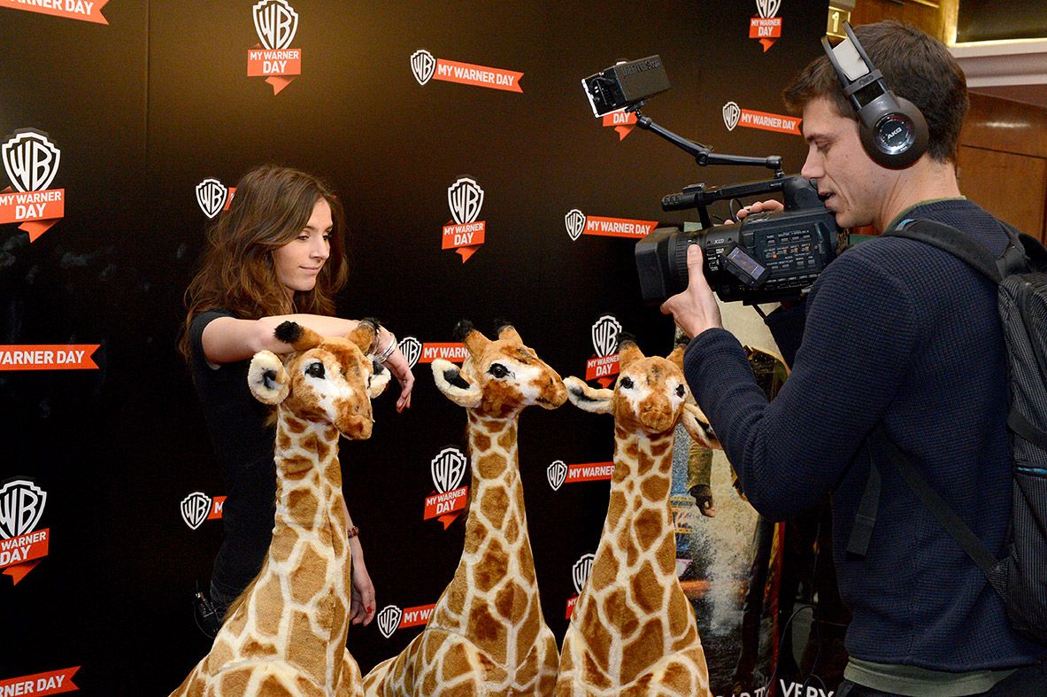 Invitée posant avec trois girafes en peluche devant un cameraman, mur My Warner Day