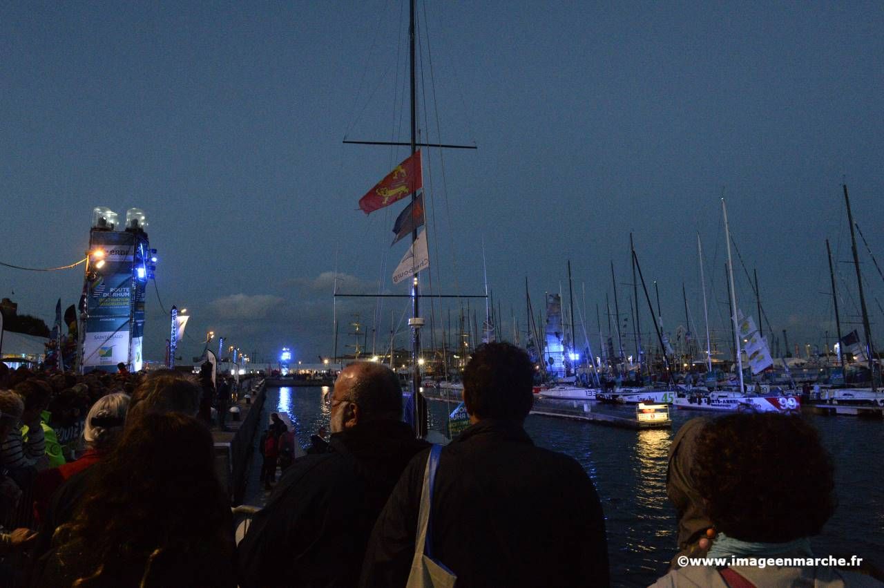 Foule de visiteurs au crépuscule sur les quais du port, mâts illuminés