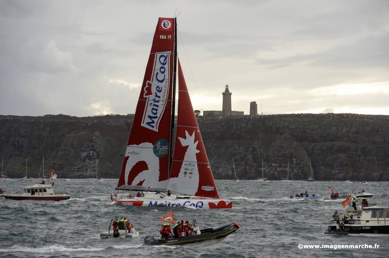Monocoque Maître CoQ voile rouge et blanche, phare sur la falaise