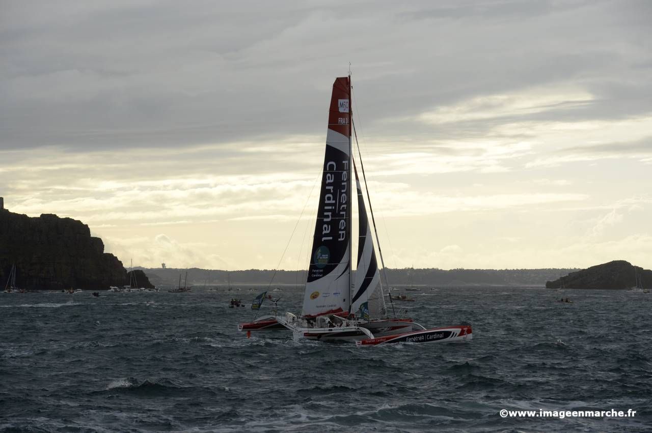 Trimaran à contre-jour entre deux rochers sous un ciel chargé