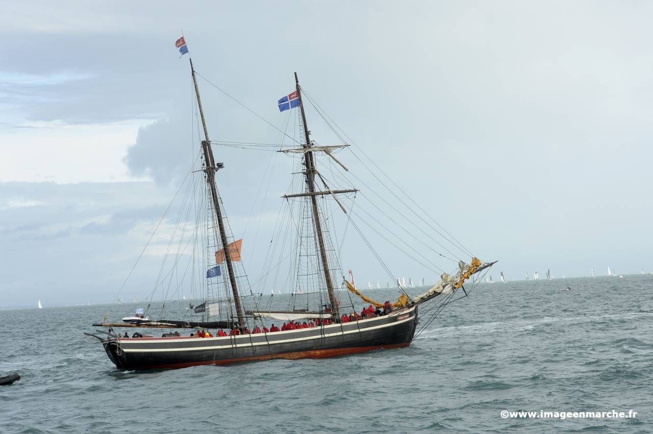 Goélette à deux mâts naviguant parmi les spectateurs