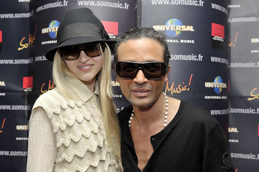 Duo en lunettes noires posant devant le mur de logos So Music