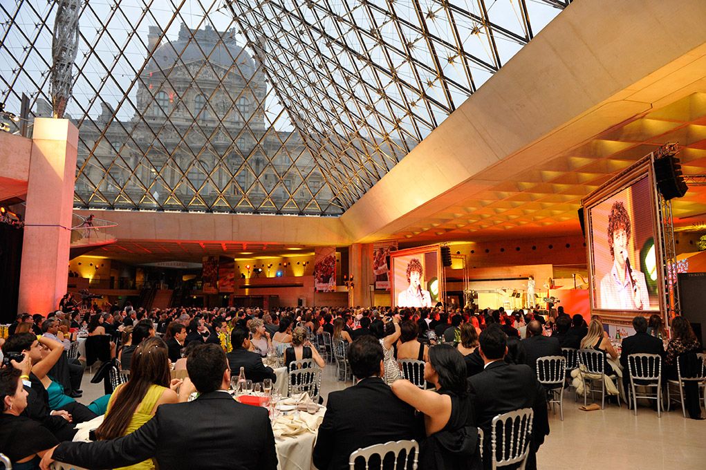Dîner de gala sous la pyramide du Louvre, tables pleines et écrans géants